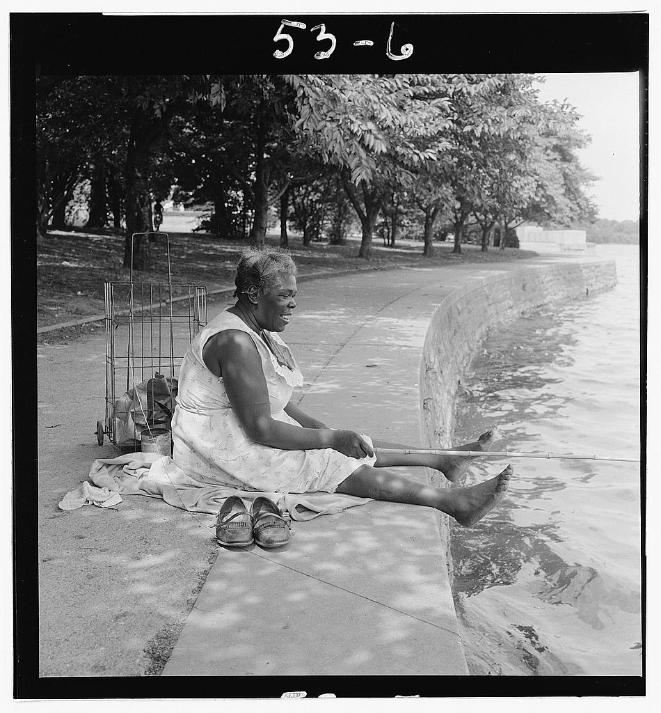 [African American woman, seated on ground, fishing, at the Tidal Basin, Washington, D.C.]